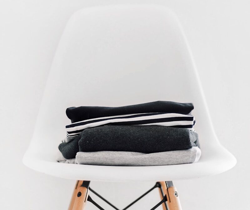 pile of black, white, and gray textiles on white padded chair with brown frame