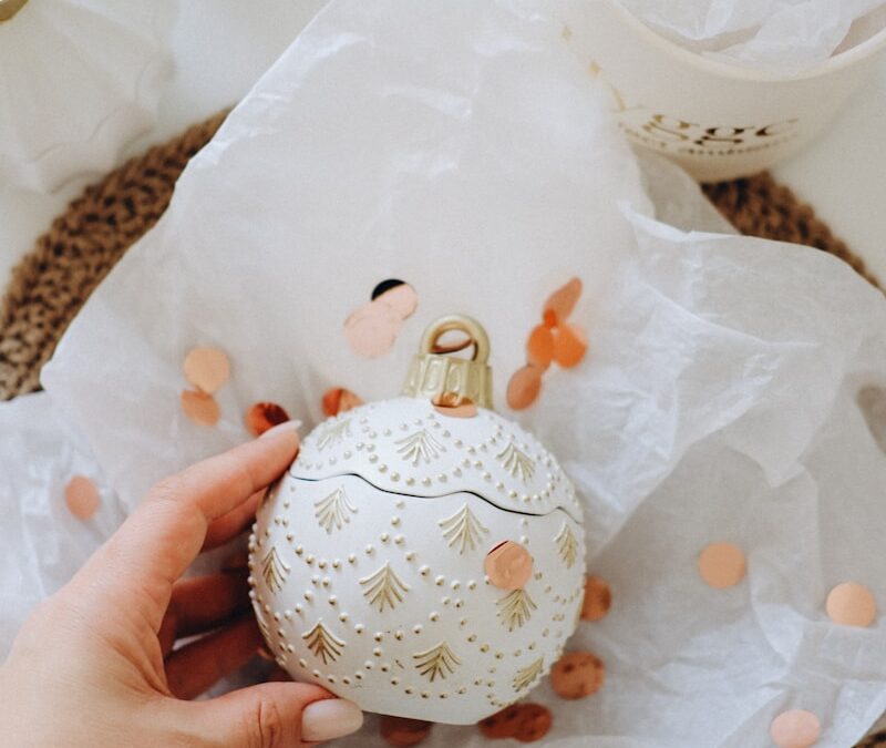 Hand holding decorative white bauble with gold accents